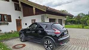 A black SUV parked in front of a white building with a traditional design, including wooden shutters and a tiled roof. - Apartment 2, 55sqm, balcony, kitchenette, 2 bedrooms, 1 living room, WLAN (Ruhpolding)