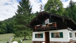 Un edificio de estilo chalet con balcón, rodeado de un área cercada y árboles.