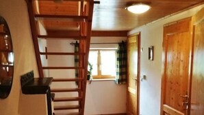 Una escalera de madera que lleva al segundo piso, suelo de baldosas y una puerta con un ventanal al fondo.