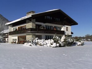 A modern two-story house with a stone facade, large windows, and a balcony. - Apartment Rauschberg 100 sqm, south-facing terrace, kitchen, 2 bedrooms and 1 living room, WLAN (Ruhpolding)