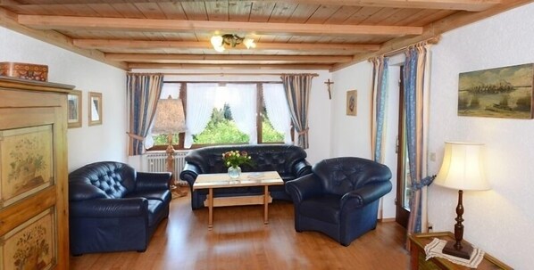 Una habitación acogedora con techo de madera, un sofá de cuero negro y una mesa de centro de madera, además de una lámpara sobre una mesita.