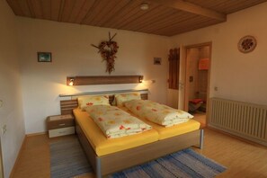 Ein Schlafzimmer mit Holzboden, einem Bett mit Blumenmuster-Bettwäsche, einem Nachttisch, einer Wandleuchte und einem Heizkörper.