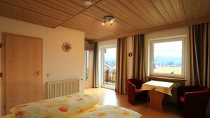 A room with two beds, a desk, a chair, a window with a view, and a wooden ceiling. - Zwei-Raum-Ferienwohnung "Kaiserblick" 46qm, Dusche/WC, Extra-Schlafraum, Küche (Reit im Winkl)