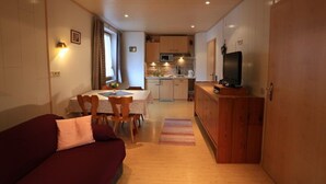 A compact living space with a dining area, kitchenette, and a TV on a wooden cabinet. - Zwei-Raum-Ferienwohnung "Kaiserblick" 46qm, Dusche/WC, Extra-Schlafraum, Küche (Reit im Winkl)