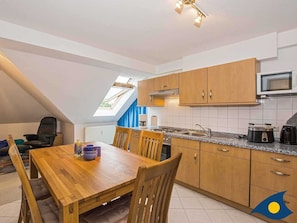 A compact kitchen with wooden cabinets, a microwave, and a toaster. There's a dining table with chairs and a small window above it.