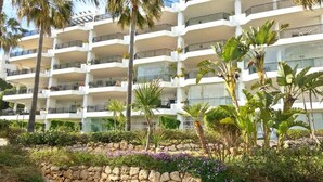 A multi-story hotel with balconies, surrounded by tropical plants and a stone wall.