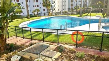 A swimming pool with a metal fence, surrounded by a grassy area and a paved walkway.