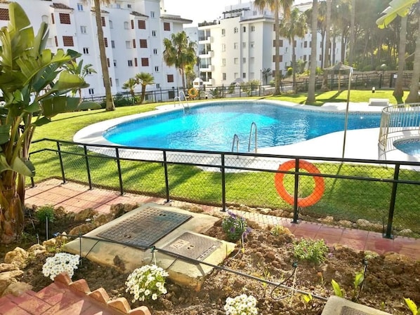 A swimming pool with a metal fence, surrounded by a grassy area and a paved walkway.