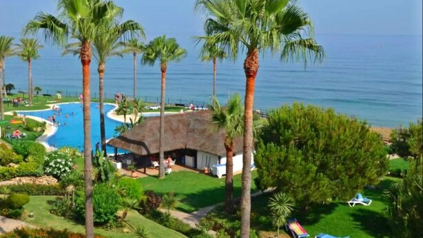 A resort with a swimming pool, palm trees, and a view of the ocean.