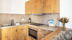 A kitchen with wooden cabinets, a stainless steel sink, a wine bottle, and a basket with books.