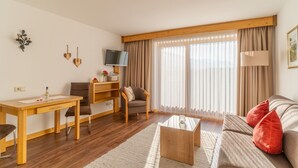 A well-lit living room with a wooden desk, a comfortable sofa, and a television on the wall. - Hausberg two-room vacation apartment 45 sqm (Reit im Winkl)