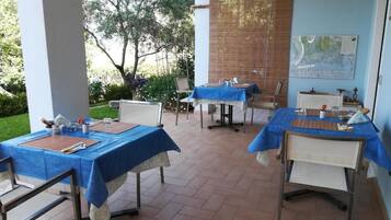 Un área de comedor al aire libre con mesas cubiertas de manteles azules, sillas y un mapa en la pared.
