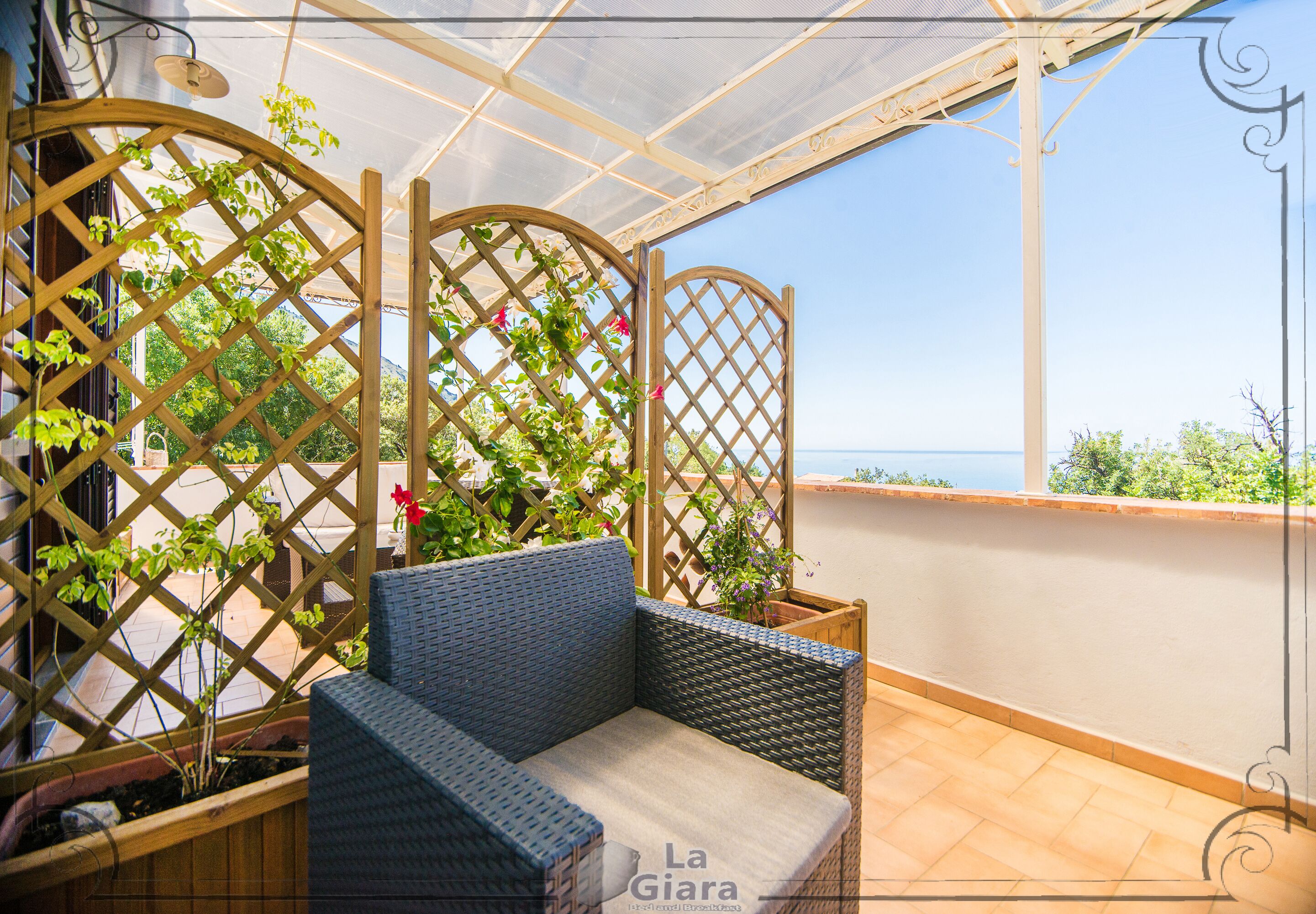 Un sofá de mimbre con un cojín, una estructura de celosía de madera y vista al mar.