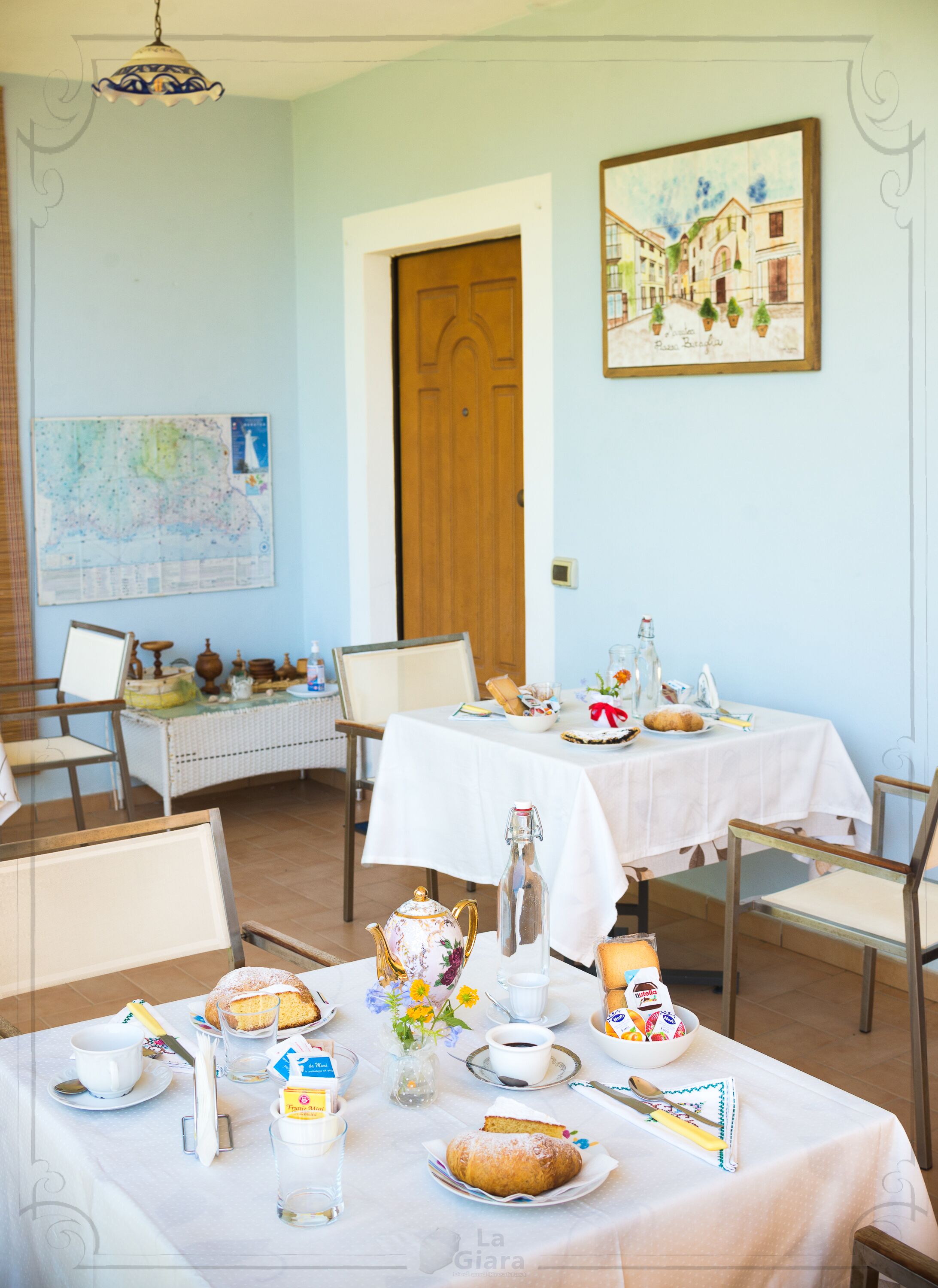 A dining room with two tables set for breakfast, featuring pastries, coffee, and a vase of flowers.