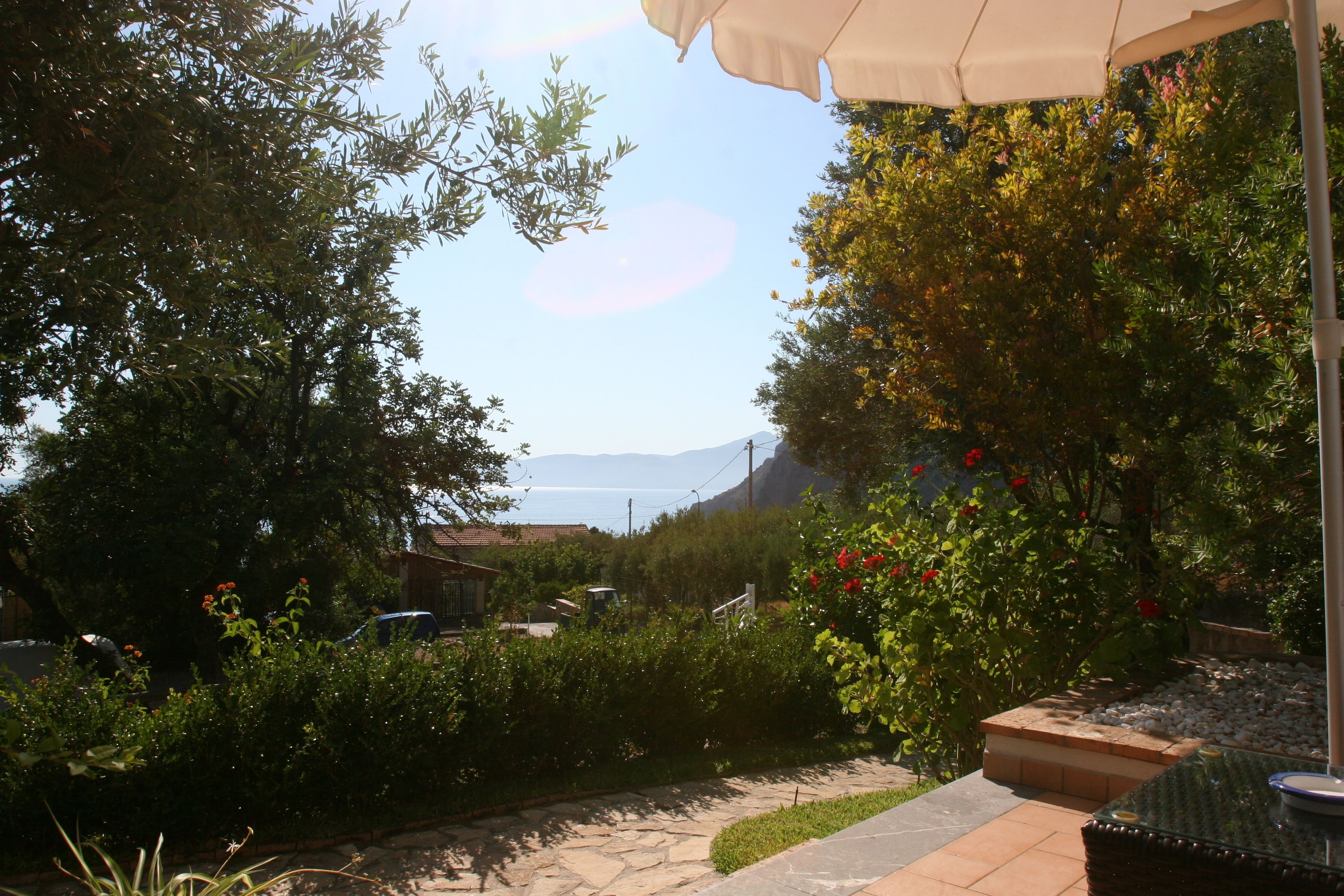 A garden with a table and chairs, a pathway, and a view of the sea.
