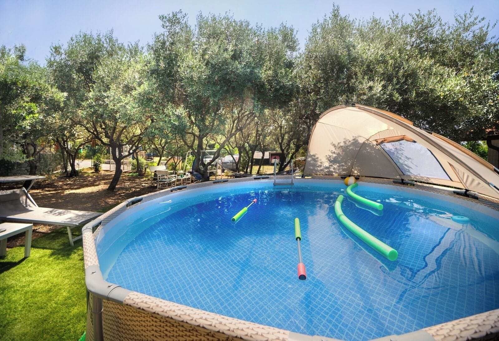 An outdoor swimming pool with a covered area, surrounded by trees and outdoor furniture.