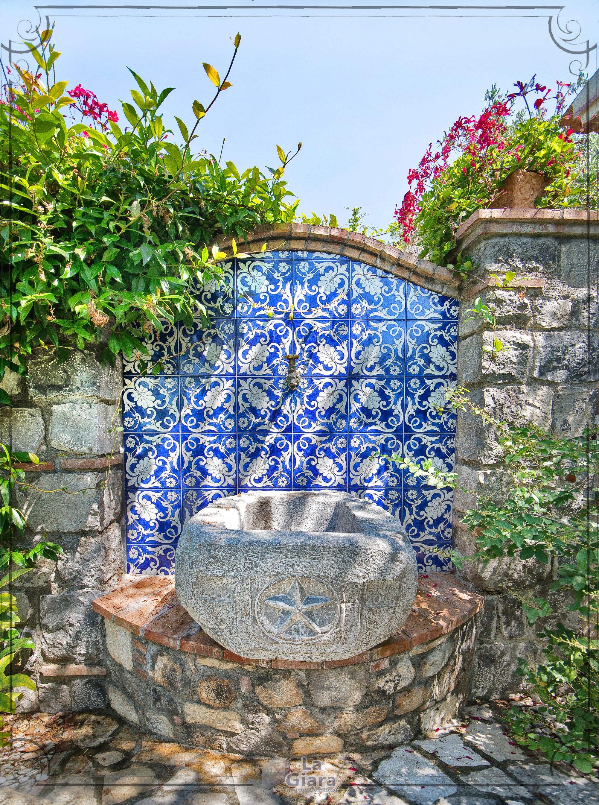 A stone fountain with a star emblem, surrounded by a stone wall and a blue and white tiled wall with floral patterns.