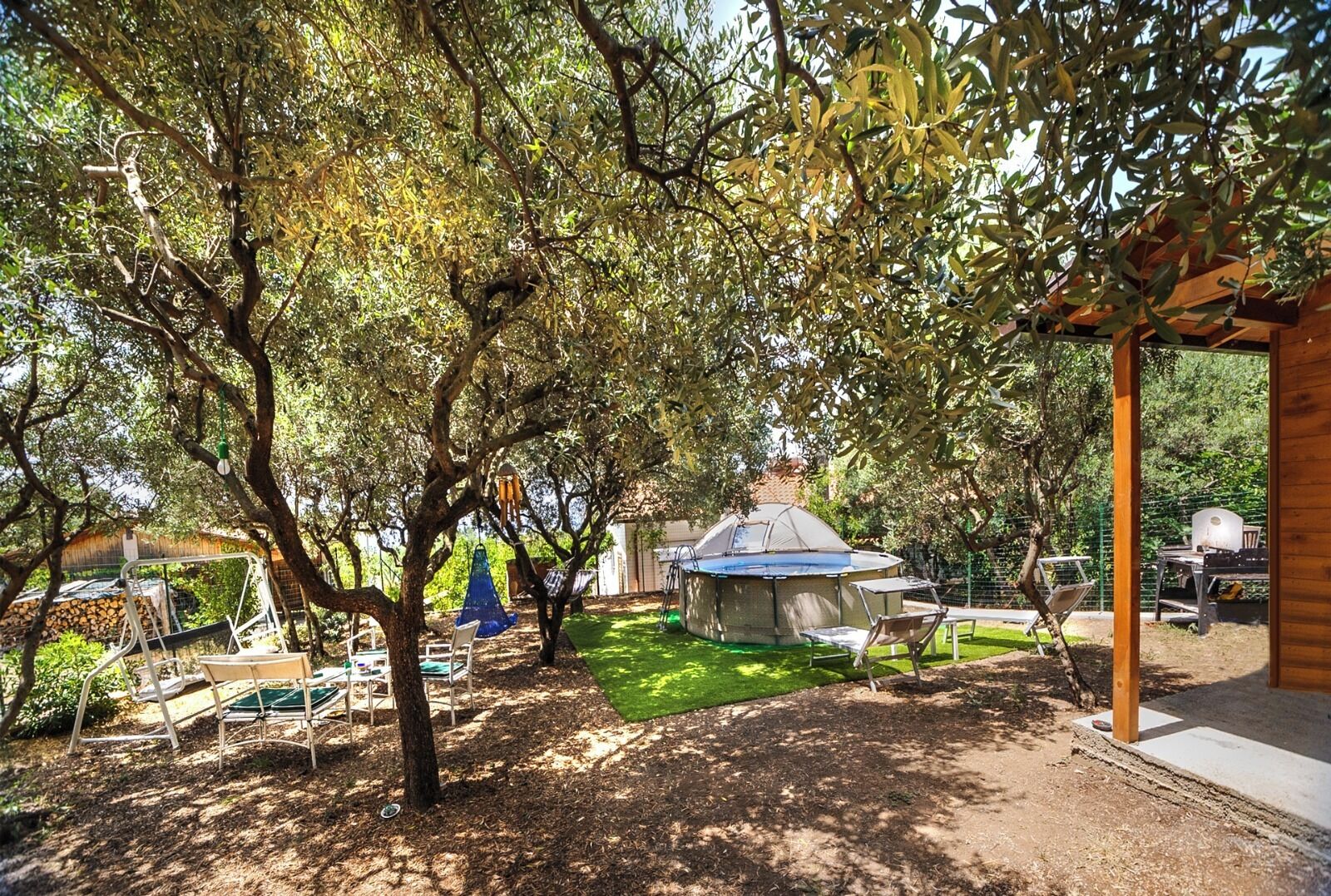 A covered outdoor area with a dome structure, surrounded by trees and outdoor furniture.