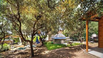 A covered outdoor area with a dome structure, surrounded by trees and outdoor furniture.