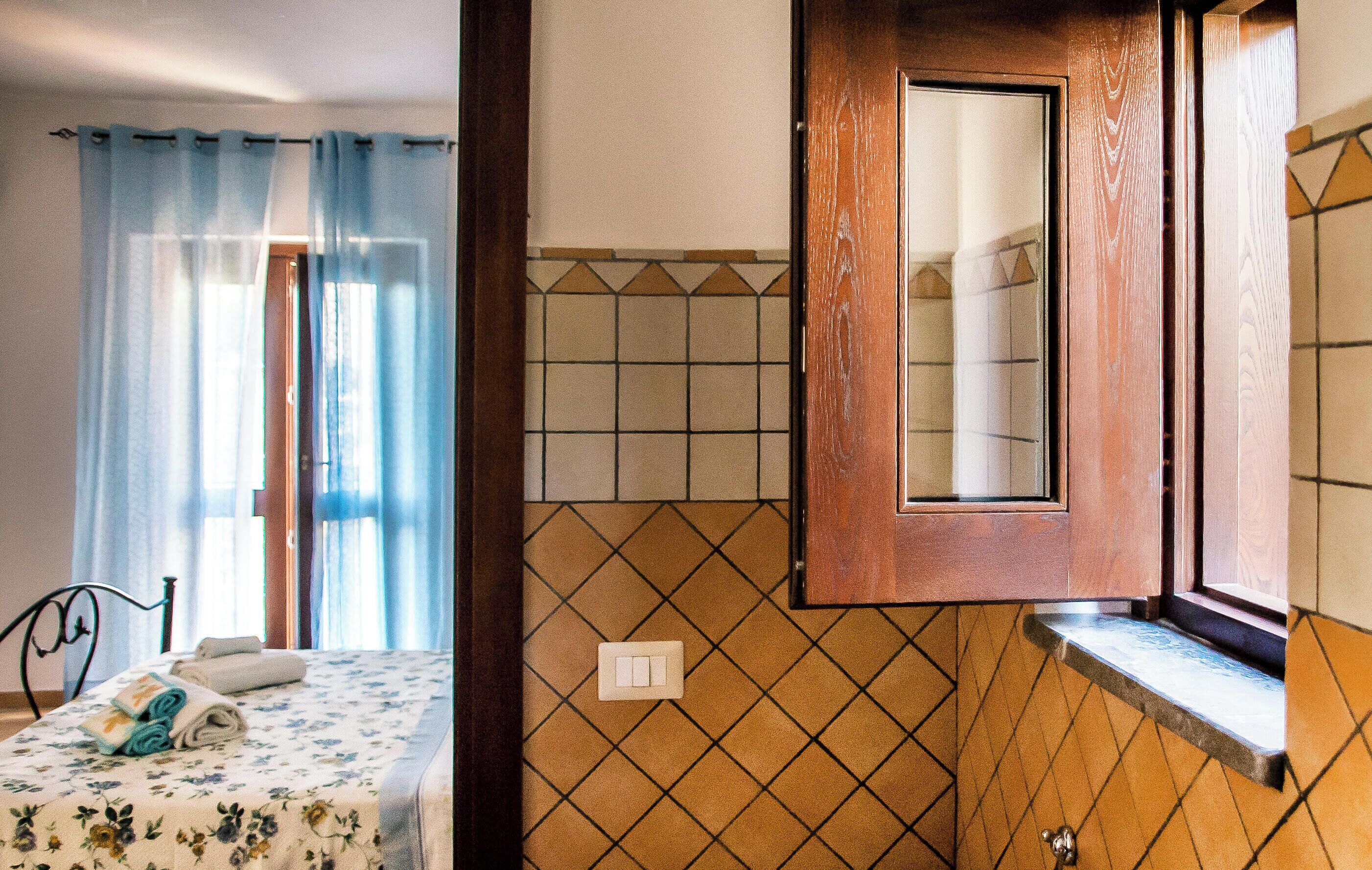 Una camera da letto con un letto, tende e un bagno con parete piastrellata e porta in legno.