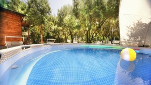 A swimming pool with a tiled surface, surrounded by trees and a wooden structure. - B&B La Giara (Maratea)
