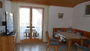 En matplats med ett träbord och stolar, en träbänk och en tv som står på ett träskåp.