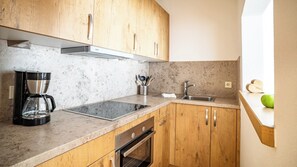 A compact kitchen with wooden cabinets, a built-in oven, a coffee maker, and a sink. - (4) Wilder Kaiser Zwei-Raum-Ferienwohnung 55 qm (Reit im Winkl)