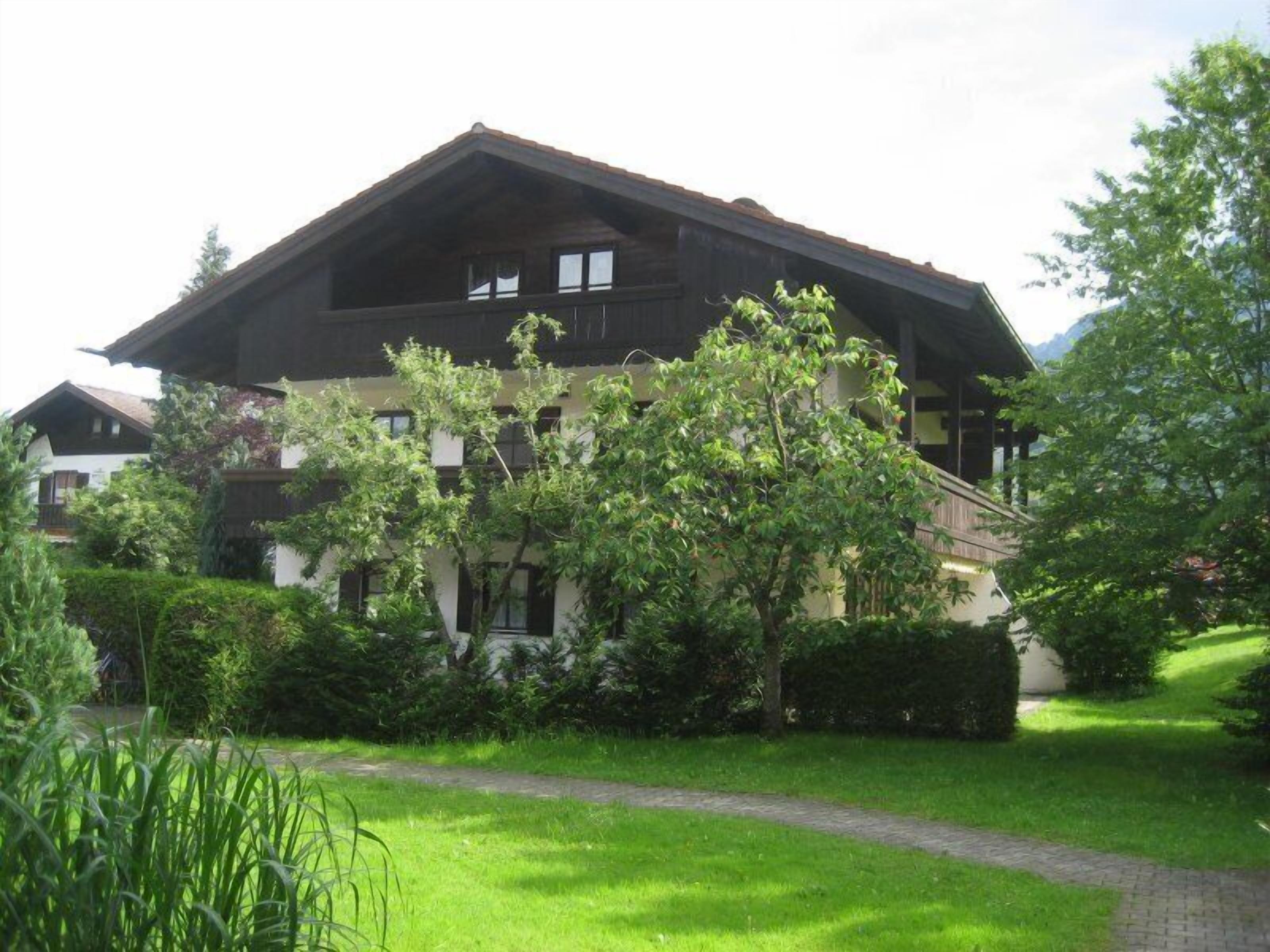 A traditional chalet-style building with a sloped roof, surrounded by lush greenery and a well-maintained lawn.