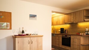 Eine Küche mit Holzausstattung, einer Arbeitsplatte, einer Flasche, Gläsern und einer Korktafel an der Wand.