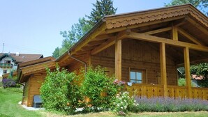 A wooden cabin with a porch, surrounded by a well-maintained garden with various plants and flowers. - Holzblockhaus Hochries ***** (Rimsting)