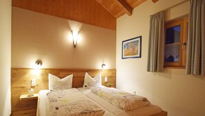 Ein Schlafzimmer mit einem Holzkopfstück, zwei Nachttischen mit Lampen, einem Bett mit floralem Bettzeug, einem Fenster mit Vorhängen und einem Gemälde an der Wand.