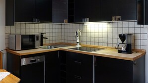 Eine moderne Küche mit schwarzen Schränken, einer Edelstahl-Spüle, einem Geschirrspüler von Bosch und einer Kaffeemaschine.