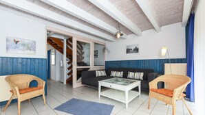 A living room with wicker chairs, a sofa, a coffee table, and a blue rug. - Holiday house beach pearl (Esens)