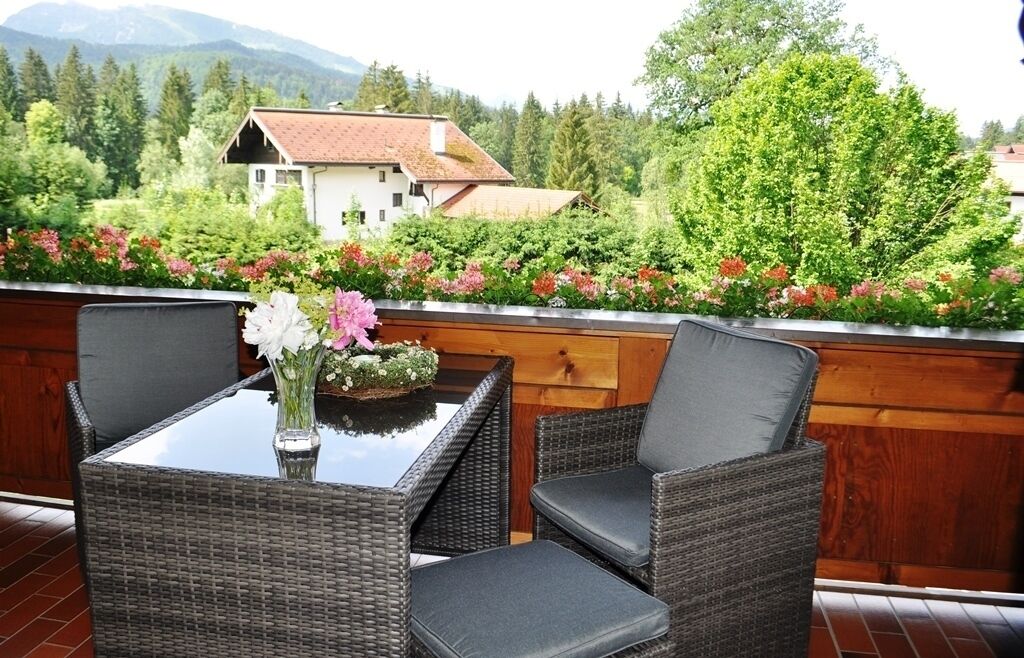 A balcony with wicker furniture, a glass table, and a vase with flowers.
