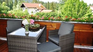 A balcony with wicker furniture, a glass table, and a vase with flowers. - Ein-Raum-Wohnung (4) 40 qm, Dusche/WC, Couch, Küchenzeile, Balkon (Reit im Winkl)