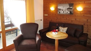 A cozy room with a wooden ceiling, a brown leather sofa, a small round table with a bottle and glasses, and a window with a view of a building.