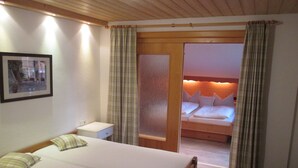 A bedroom with a large bed, a bedside table, a nightstand, and a door leading to another room.