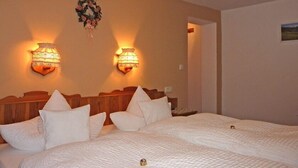A hotel room with two beds, each with white bedding and pillows. There are two wall-mounted lamps on either side of the bed, and a decorative wreath above the lamps. - Thomanhof Ferienwohnung (Ramsau bei Berchtesgaden)