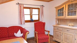 A cozy room with a red sofa, a wooden dining table, a red chair, and a wooden cabinet with glass doors. - Thomanhof Ferienwohnung (Ramsau bei Berchtesgaden)