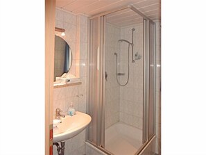 A bathroom with a glass-enclosed shower, a sink with a mirror above it, and a shelf with toiletries. - Thomanhof Ferienwohnung (Ramsau bei Berchtesgaden)