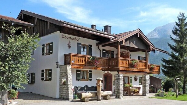 A two-story building with a balcony, stone pillars, and a mountain backdrop. - Thomanhof Ferienwohnung (Ramsau bei Berchtesgaden)