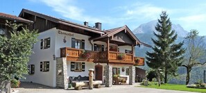 A two-story building with a balcony, stone pillars, and a mountain backdrop. - Thomanhof Ferienwohnung (Ramsau bei Berchtesgaden)