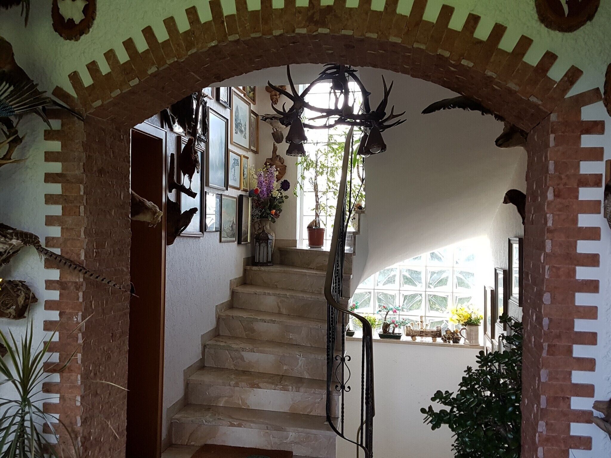 A staircase with a brick archway, surrounded by framed pictures and potted plants.