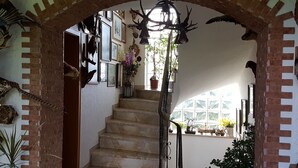 Una escala amb una llinda de rajola, envoltada de quadres amb marc i plantes en testos.