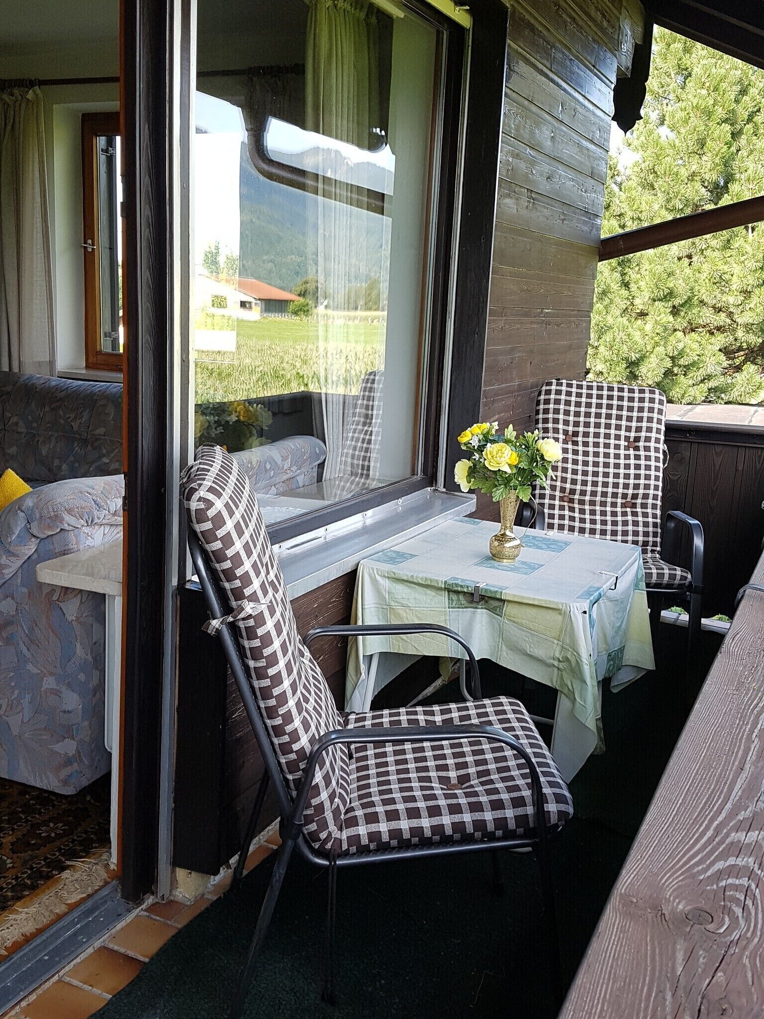 Un espace extérieur accueillant, aménagé avec une table et des chaises, un vase rempli de fleurs, et offrant une vue sur la verdure et les bâtiments.