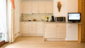 Een compacte keuken met lichte houtkleurige kastjes, een magnetron en een kleine televisie op een standaard.