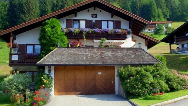 Een chalet met een houten garage, een balkon met bloemen en uitzicht op een bebost gebied.