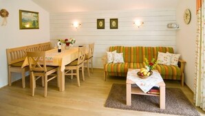Een gezellige woonkamer met een houten eettafel, stoelen, een gestreepte bank en een salontafel met fruit.