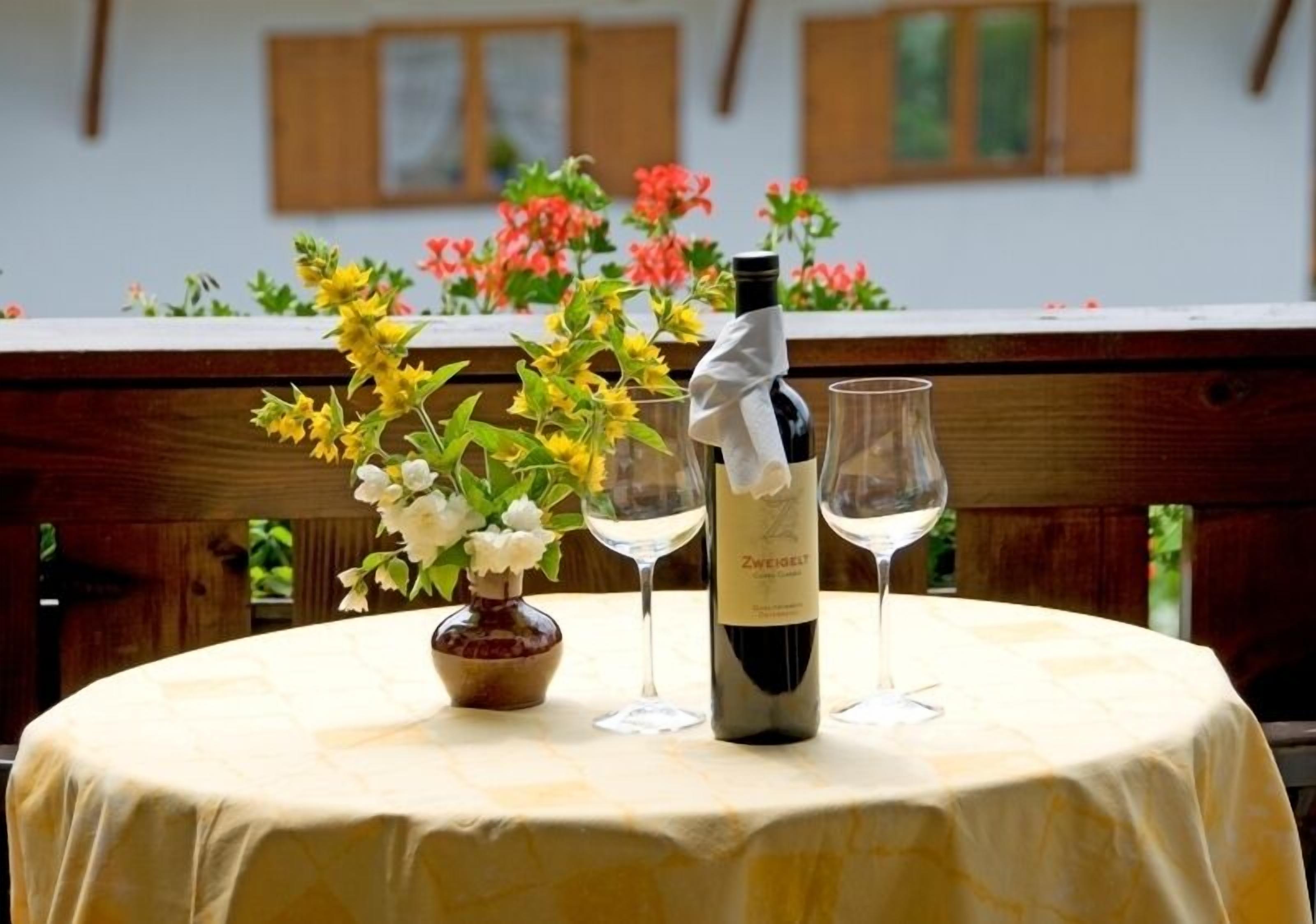 A round table with a bottle of wine and two wine glasses, surrounded by flowers.
