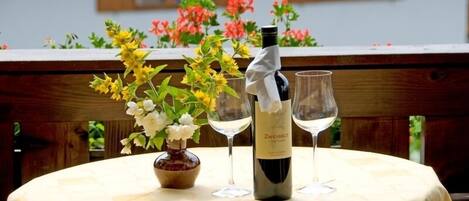 A round table with a bottle of wine and two wine glasses, surrounded by flowers.